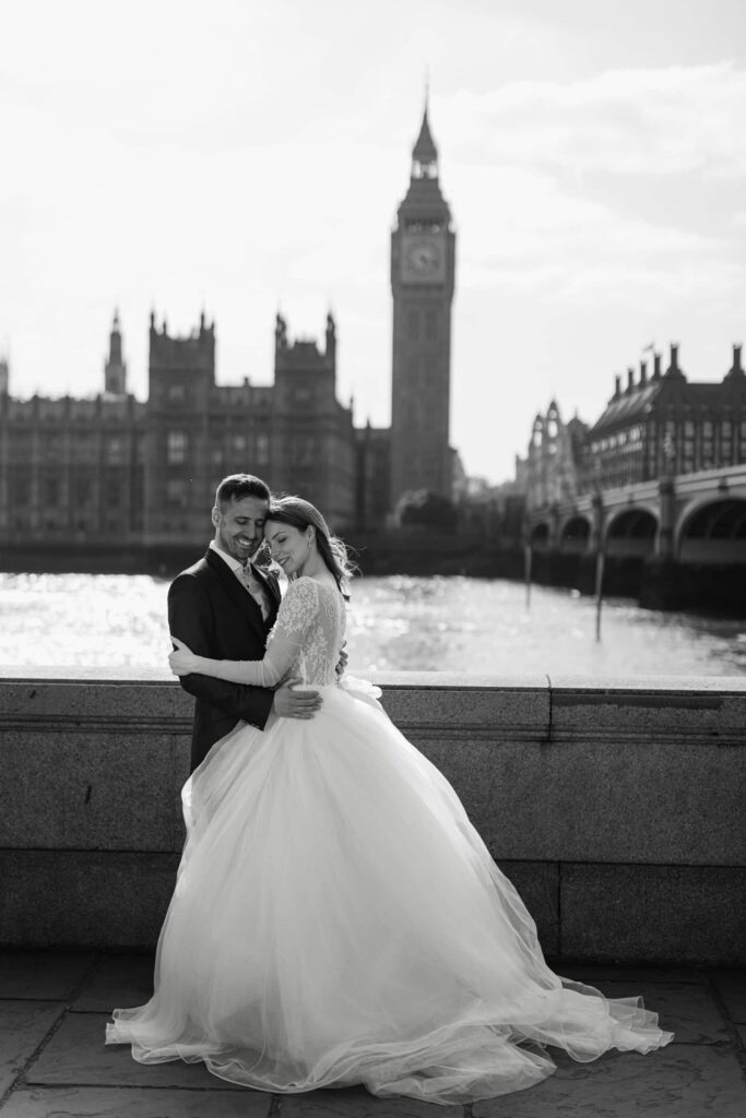 Bride and groom embracing by the Thames with Big Ben and Westminster in the background during a London wedding photoshoot.