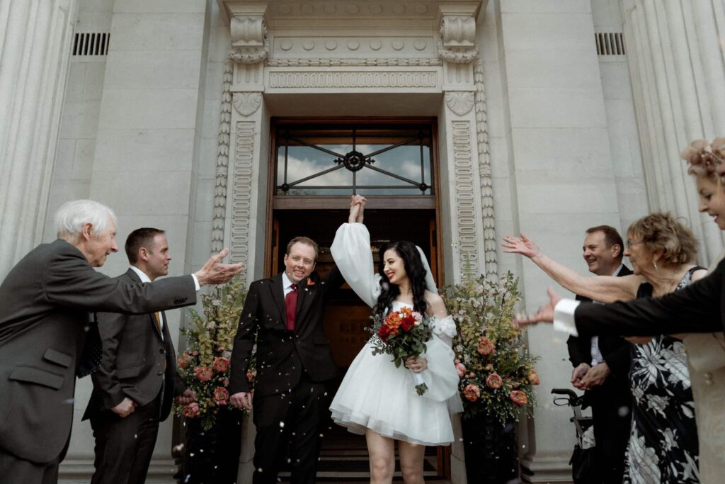 Bride and groom celebrate confetti exit outside Old Marylebone Town Hall, captured by a London wedding photographer.