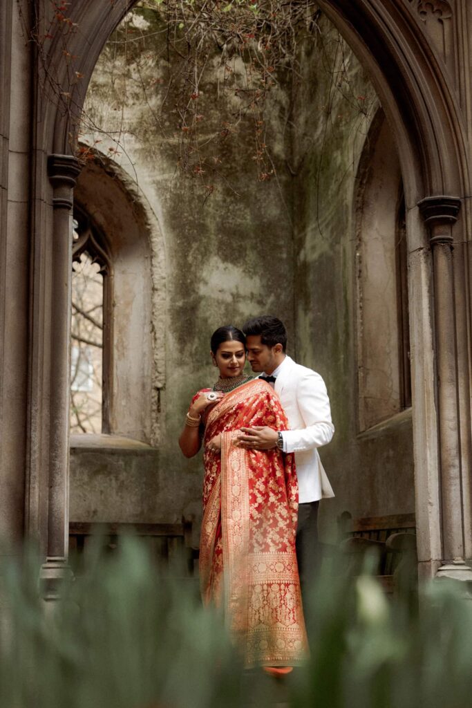 Couple embracing in St Dunstan in the East church ruins, bride in red sari, captured by a London wedding photographer.