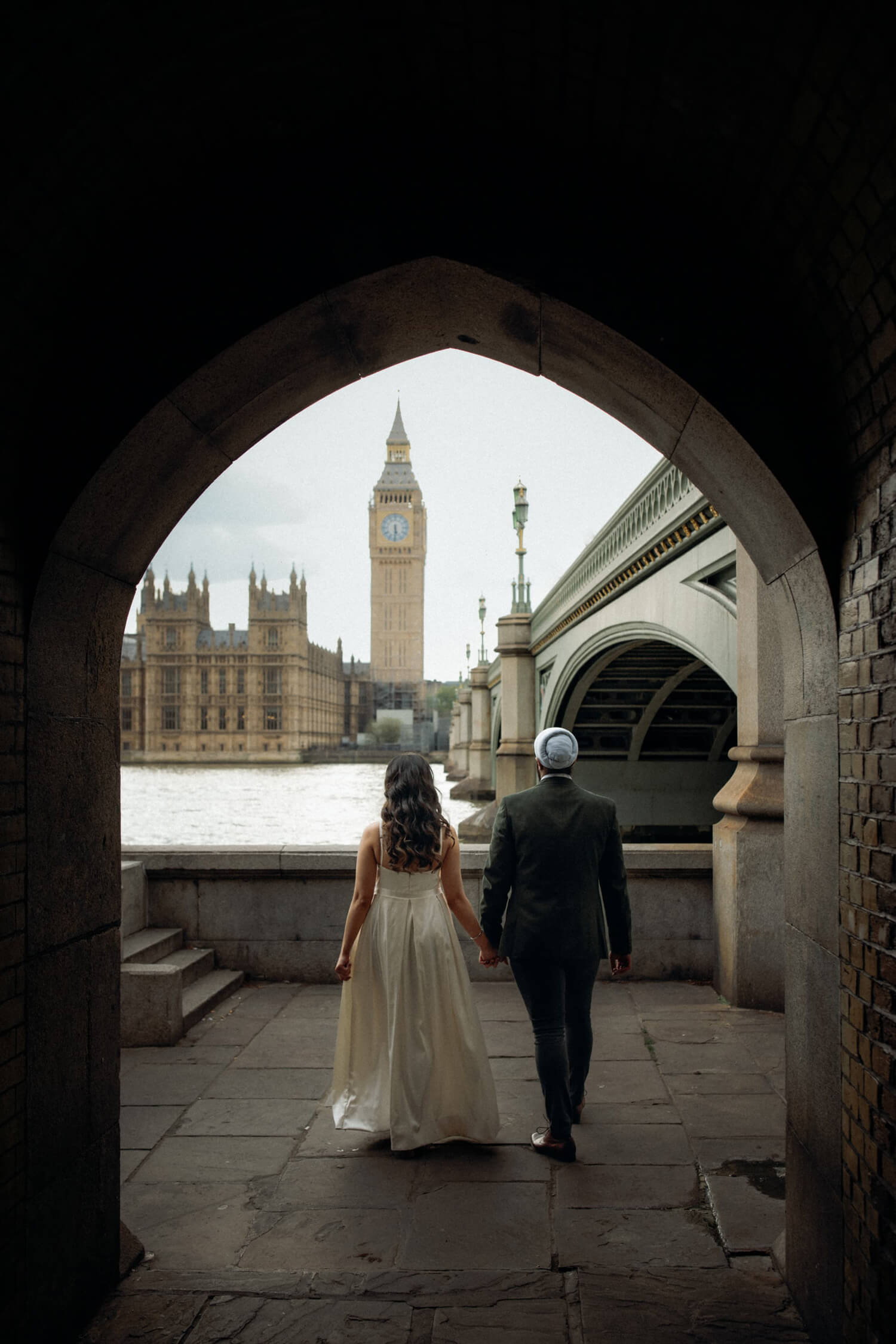 Couple walking under arch toward Big Ben and Westminster, one of the best places to elope in London.