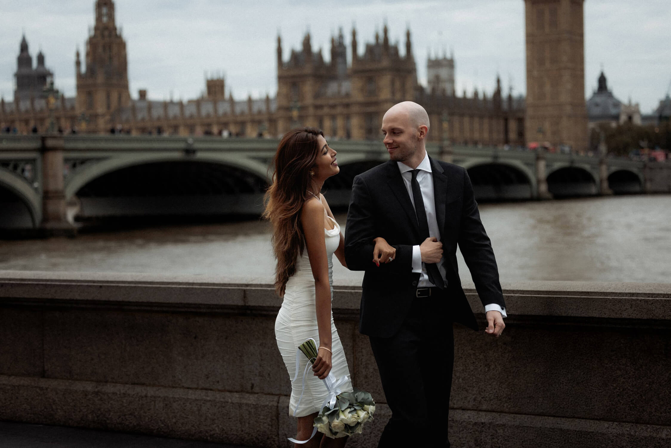 Couple walking along Southbank by the Thames with Westminster in background, one of the best places to elope in London.