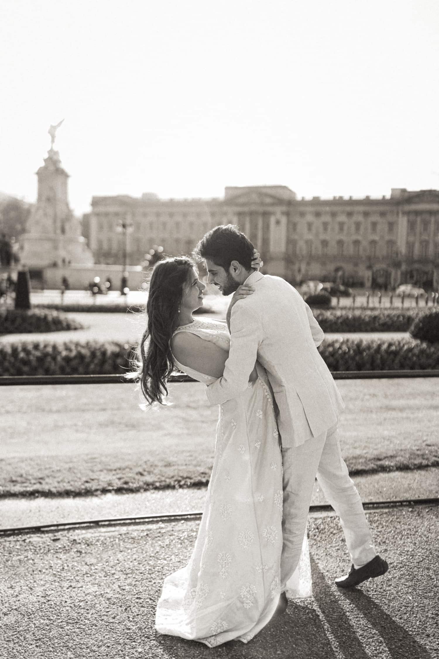 Couple dancing in front of Buckingham Palace during a pre-wedding photoshoot in London, captured in soft black and white light.