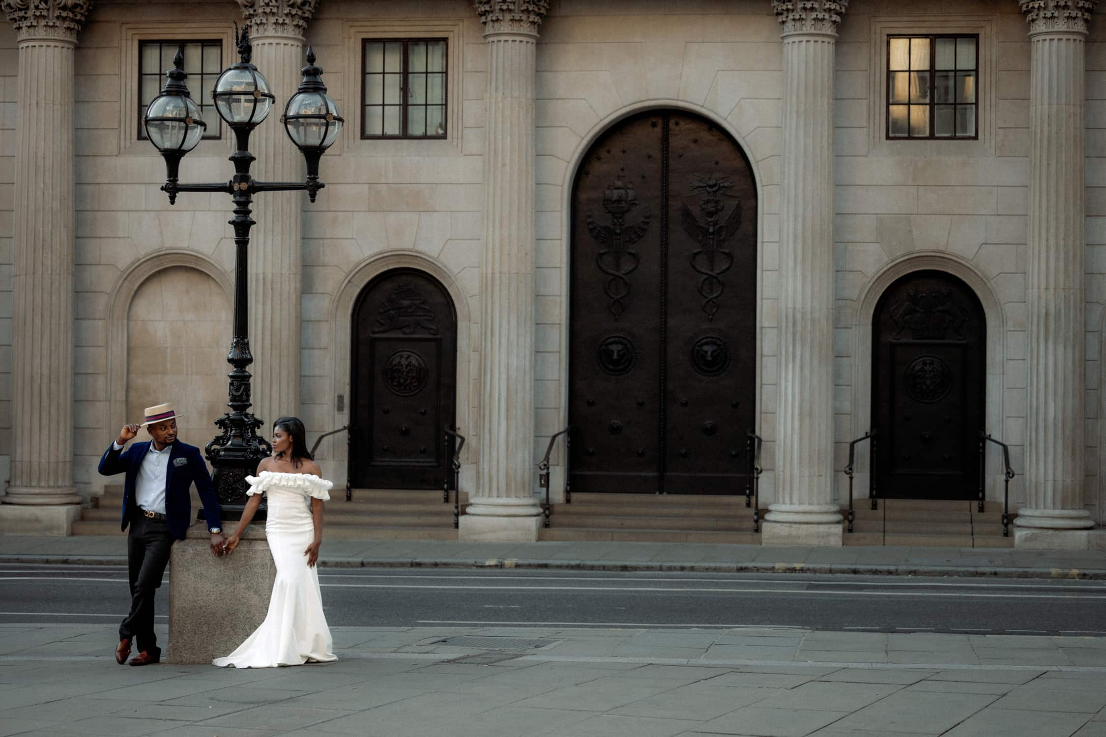 Couple in formal attire standing by grand columns and ornate doors during a pre-wedding photoshoot in London.