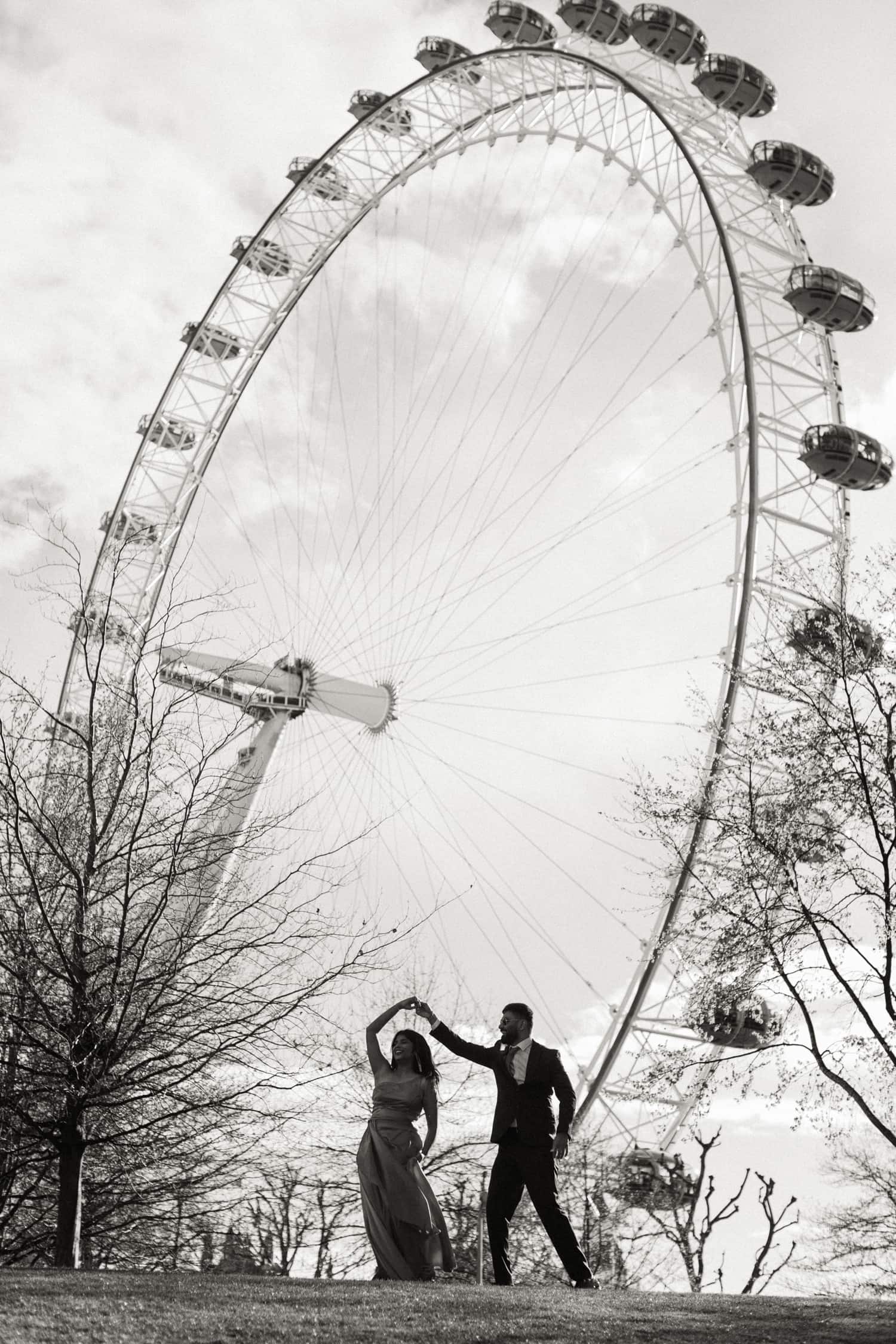 Couple dancing beneath the London Eye during a pre-wedding photoshoot in London, captured in black and white.
