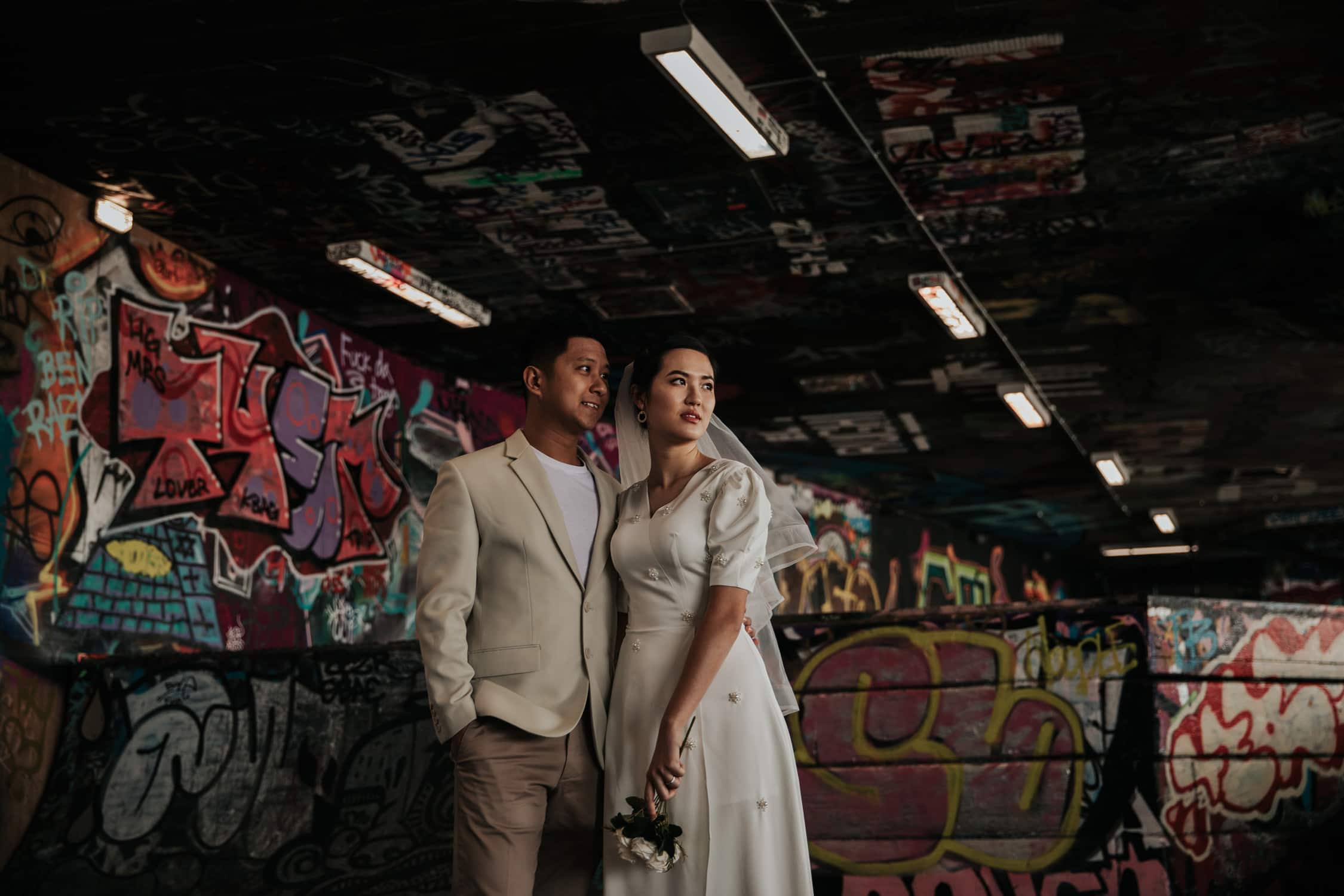 Couple in wedding attire standing in a colorful graffiti tunnel during a pre-wedding photoshoot in Westminster London.