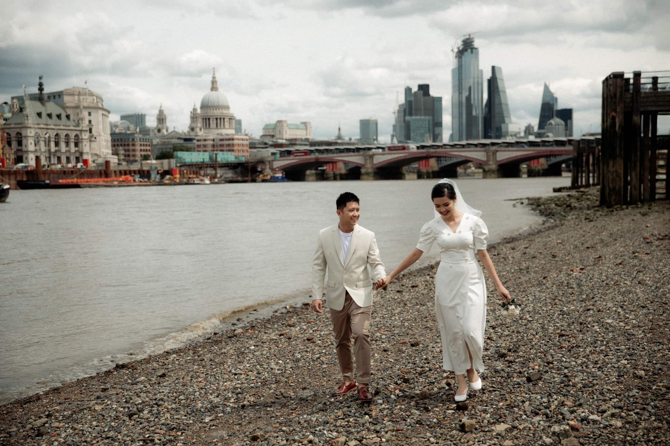 Couple walking along the Thames in Westminster with St Paul’s Cathedral and London skyline during a pre-wedding photoshoot in London.