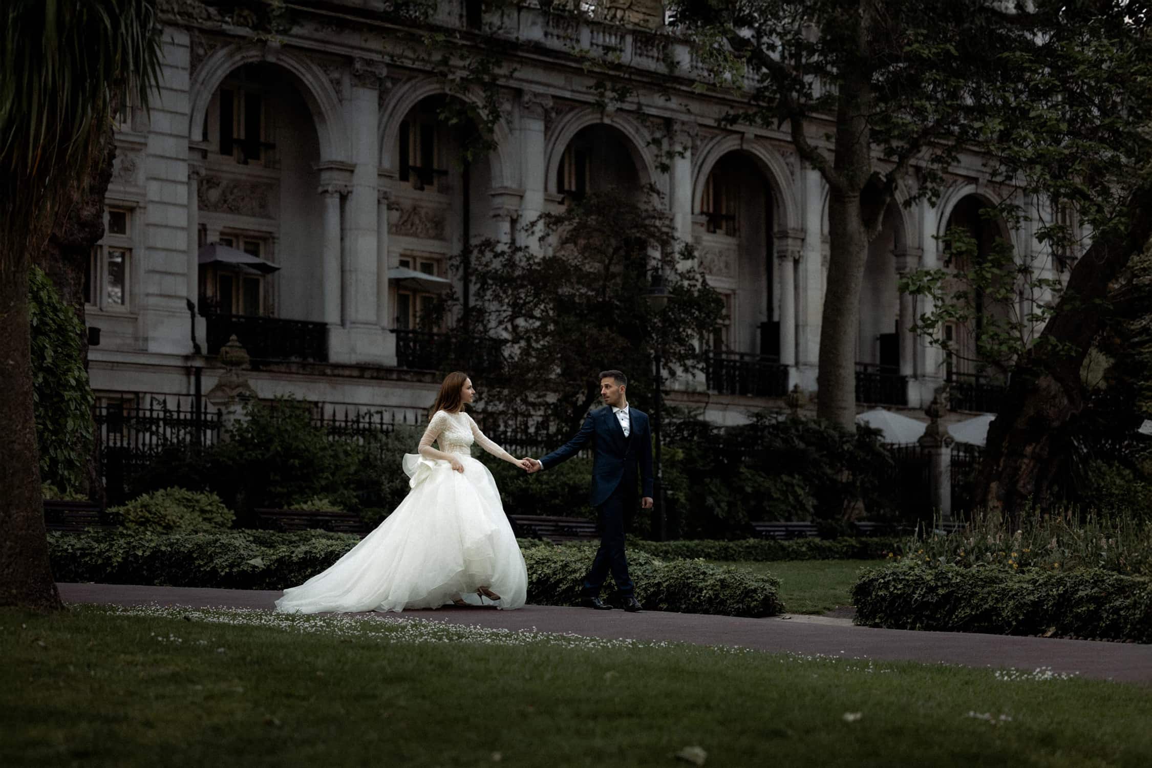 Bride and groom walking hand in hand through gardens near Leighton House during a micro wedding in London.