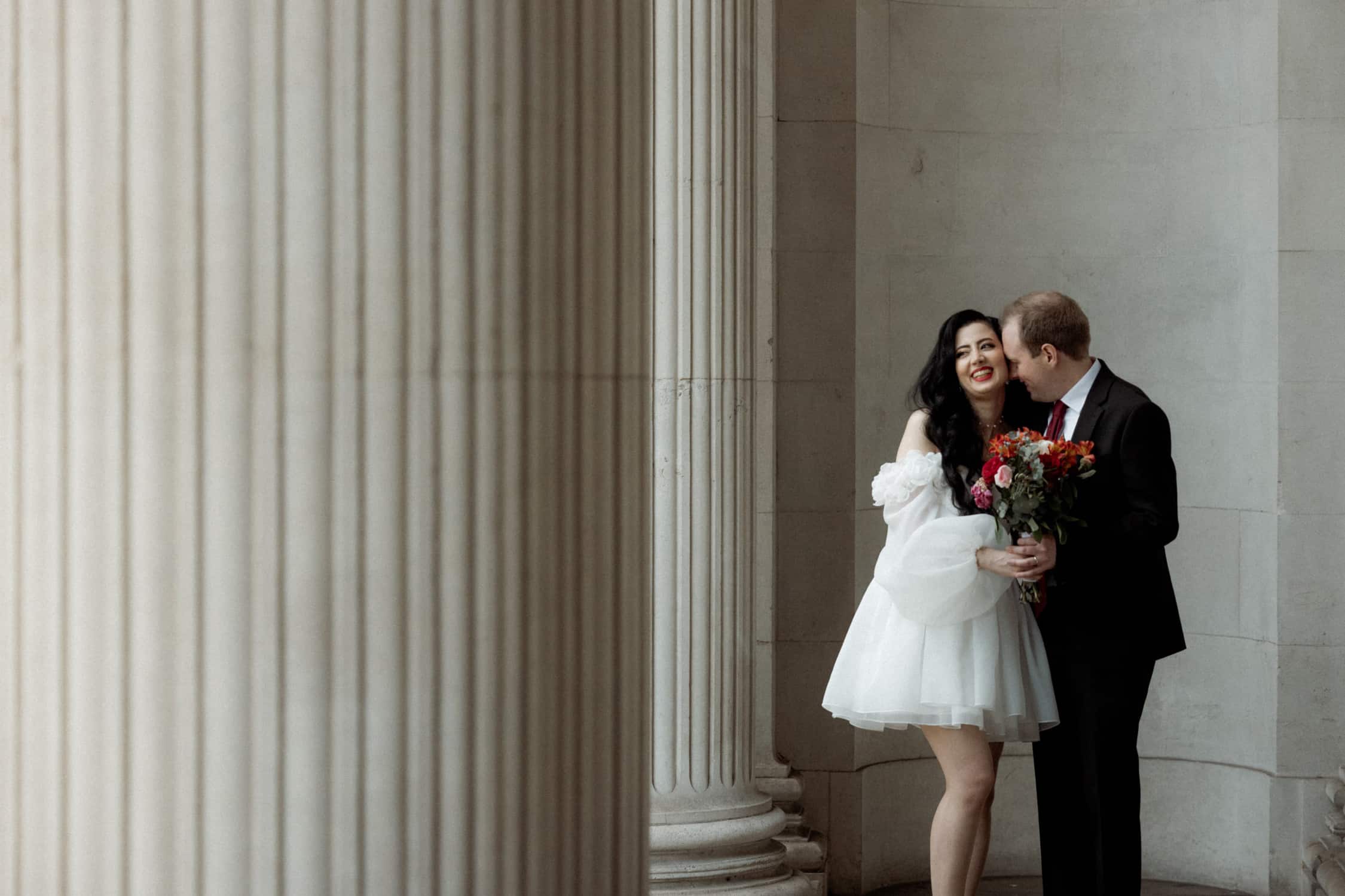 Newlywed couple sharing a quiet moment beside the grand columns of Old Marylebone Town Hall in London.