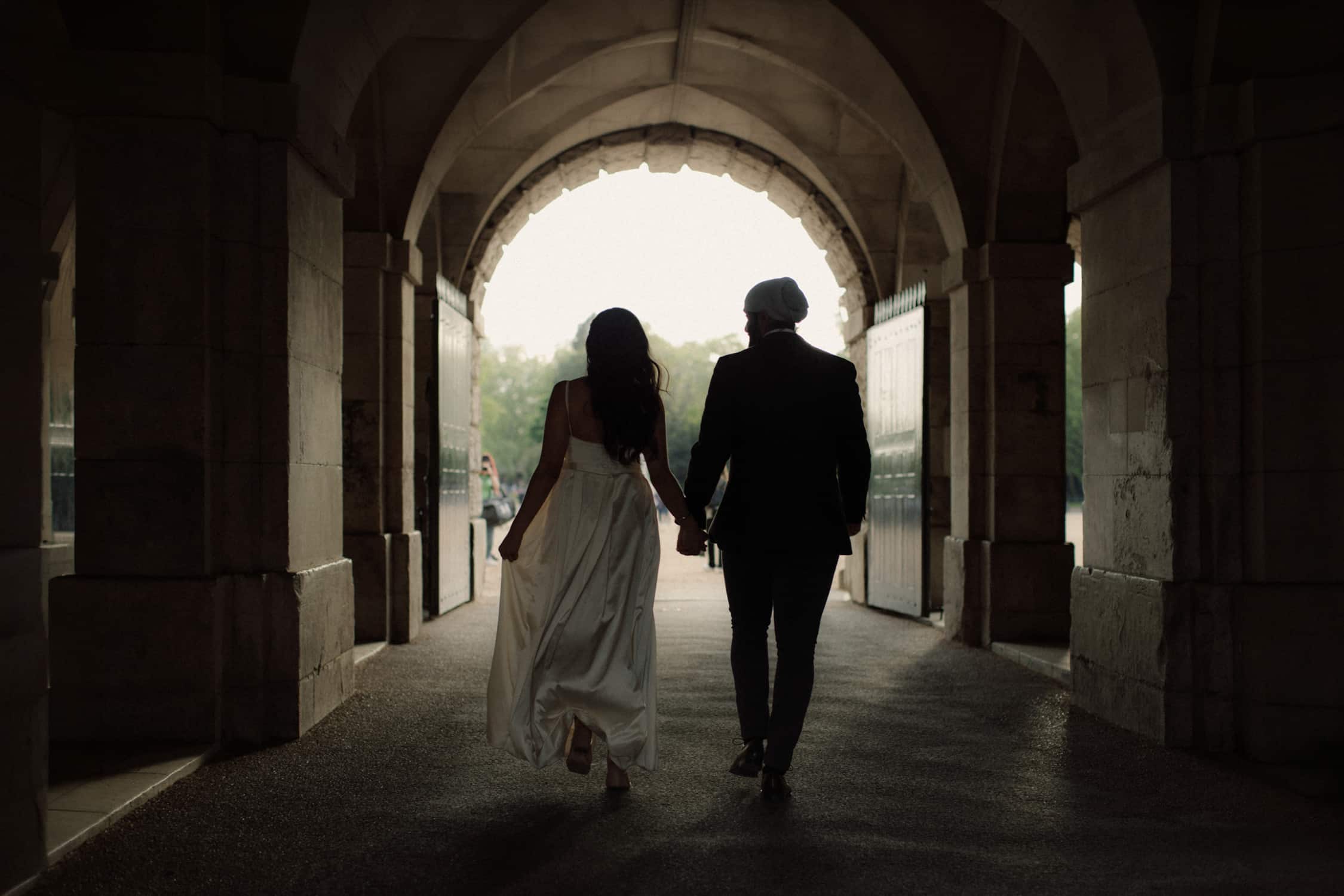 Couple holding hands beneath a historic archway during a romantic micro wedding in Westminster London.